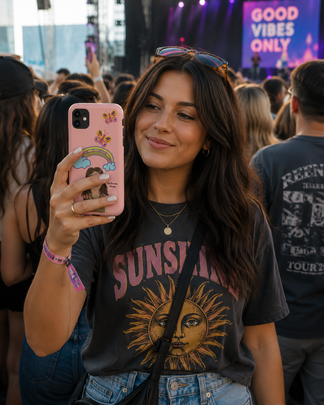 Woman at a concert holding a pink phone with a 'Good Vibes Only' sign in the background