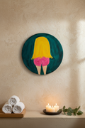 Circular wall art with a colorful depiction of a person on a beige wall, with candles and towels on a shelf below.