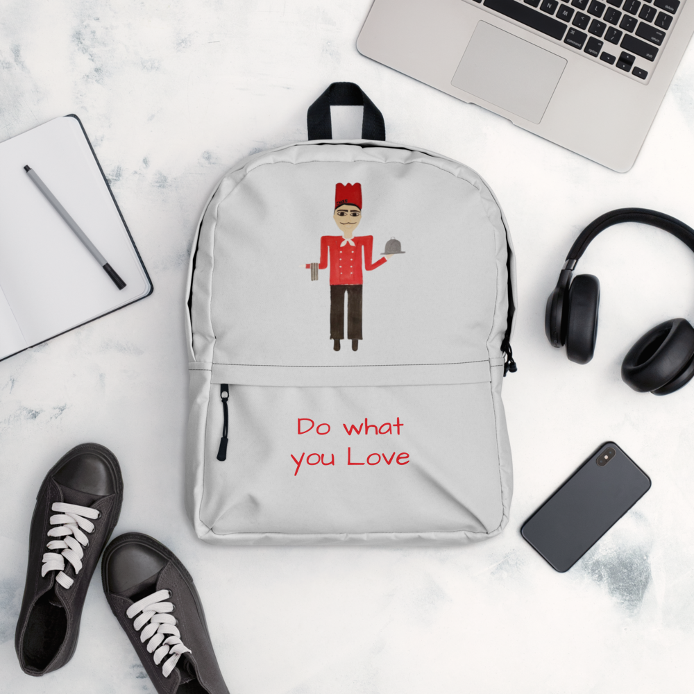Gray backpack with a design and text, placed on a marble surface with a laptop, headphones, and shoes.