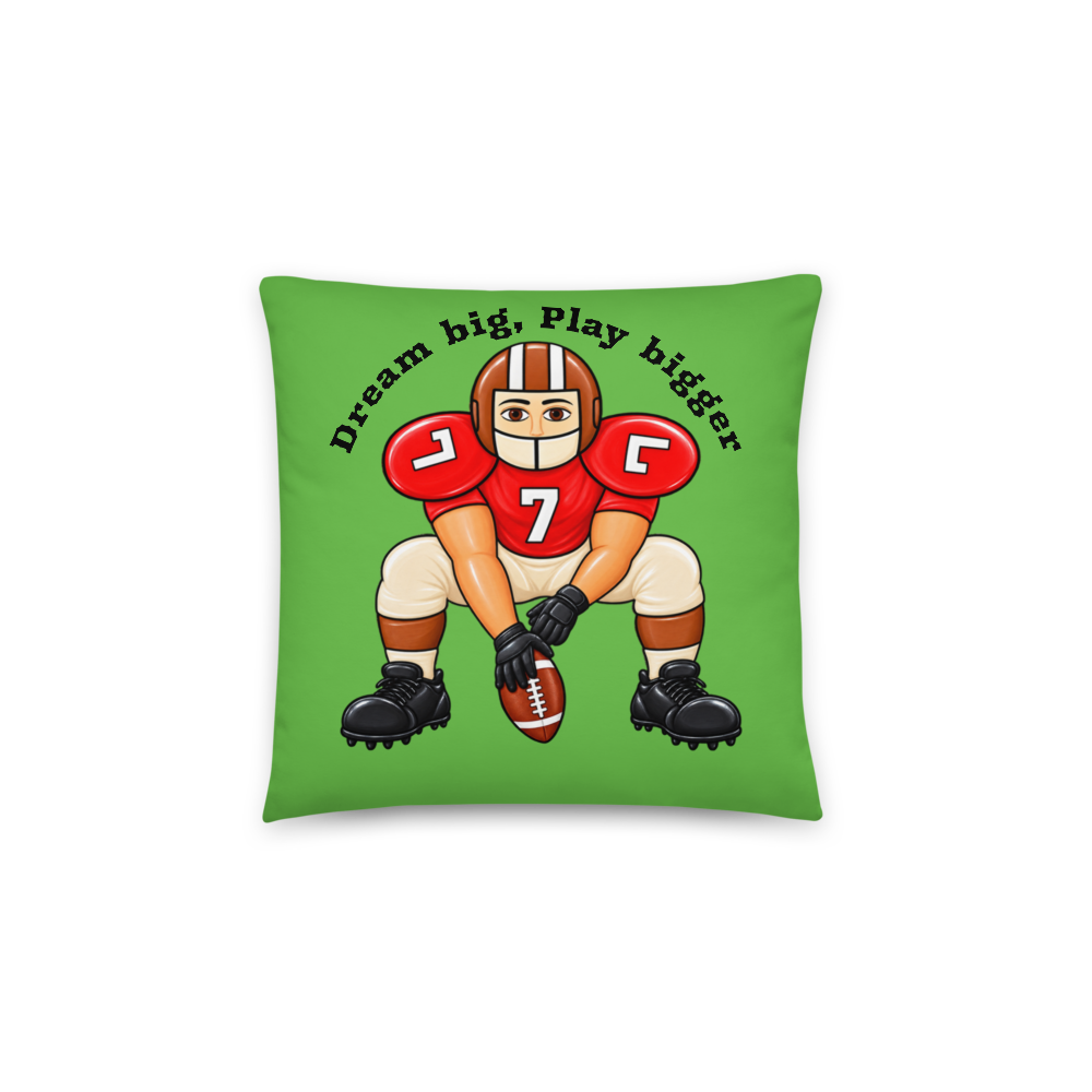 A square green throw pillow featuring a cartoon illustration of a football player in a red helmet and uniform with the number 7, holding a football, with the text 'Dream big, play bigger' above. The pillow is shown against a plain white background.
