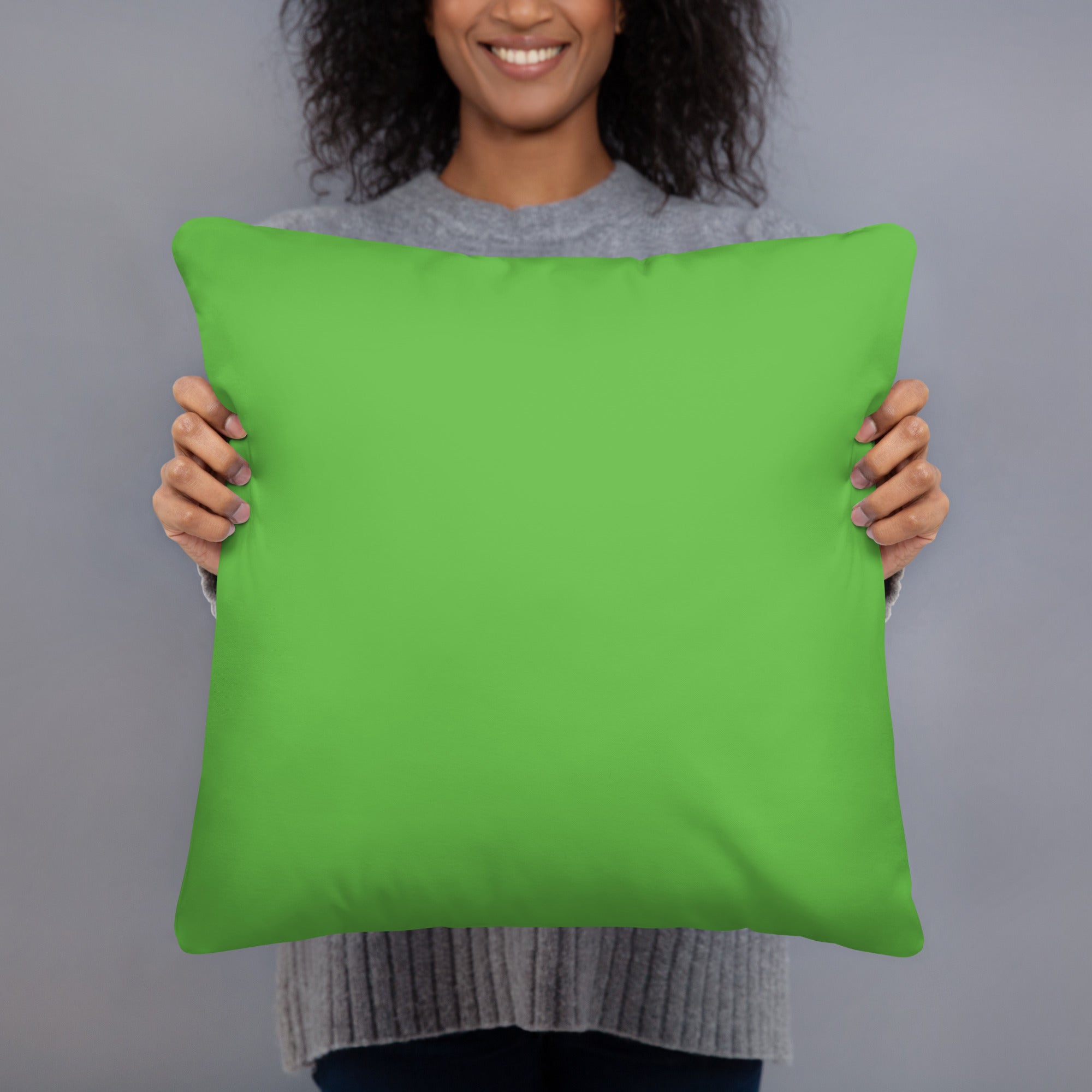 A person holding a bright lime green square throw pillow against a solid gray studio background.