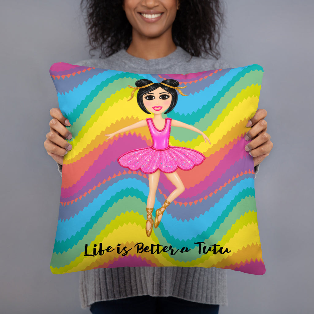 A person holding a square decorative pillow featuring a colorful rainbow wavy pattern and an illustration of a ballerina with the text 'Life is Better a Tutu'.