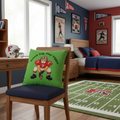 A square green throw pillow with a cartoon football player graphic and the text 'Dream big, Play bigger' is styled on a dark couch with a green blanket.