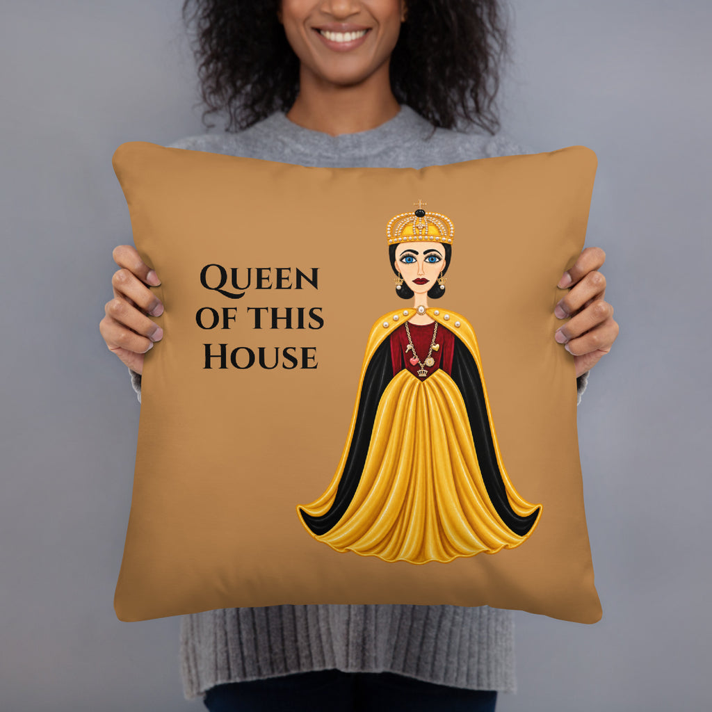 A woman holding a square tan throw pillow with a graphic of a queen in a yellow and black gown and the text 'QUEEN OF THIS HOUSE'.