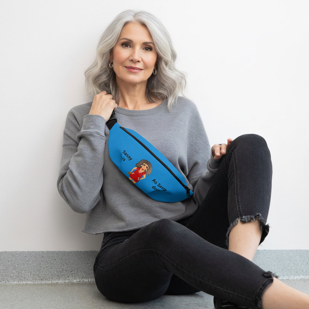 Woman sitting on the floor wearing a gray sweatshirt and black pants, holding a blue fanny pack with cartoon character design.