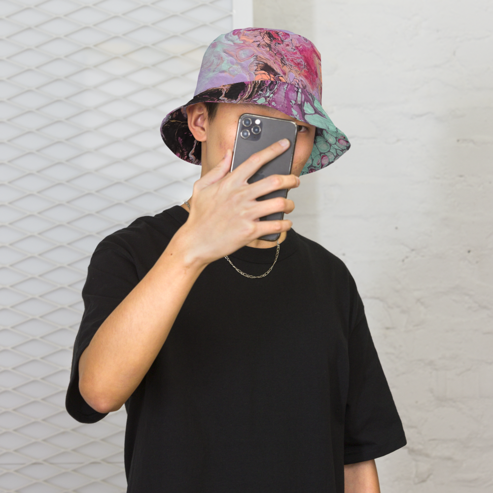 Person wearing a colorful bucket hat and black t-shirt, taking a selfie against a textured white wall.
