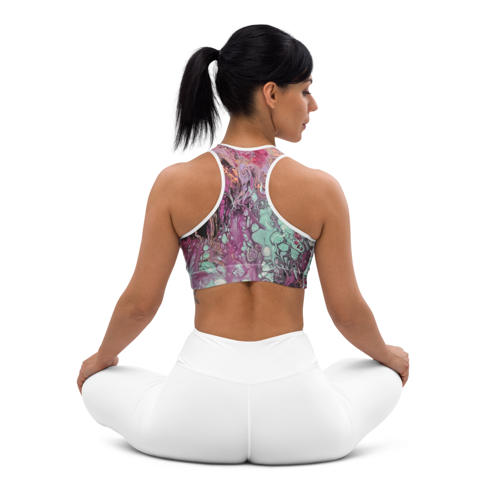 Woman sitting on a white yoga ball wearing a colorful sports bra and white pants on a white background