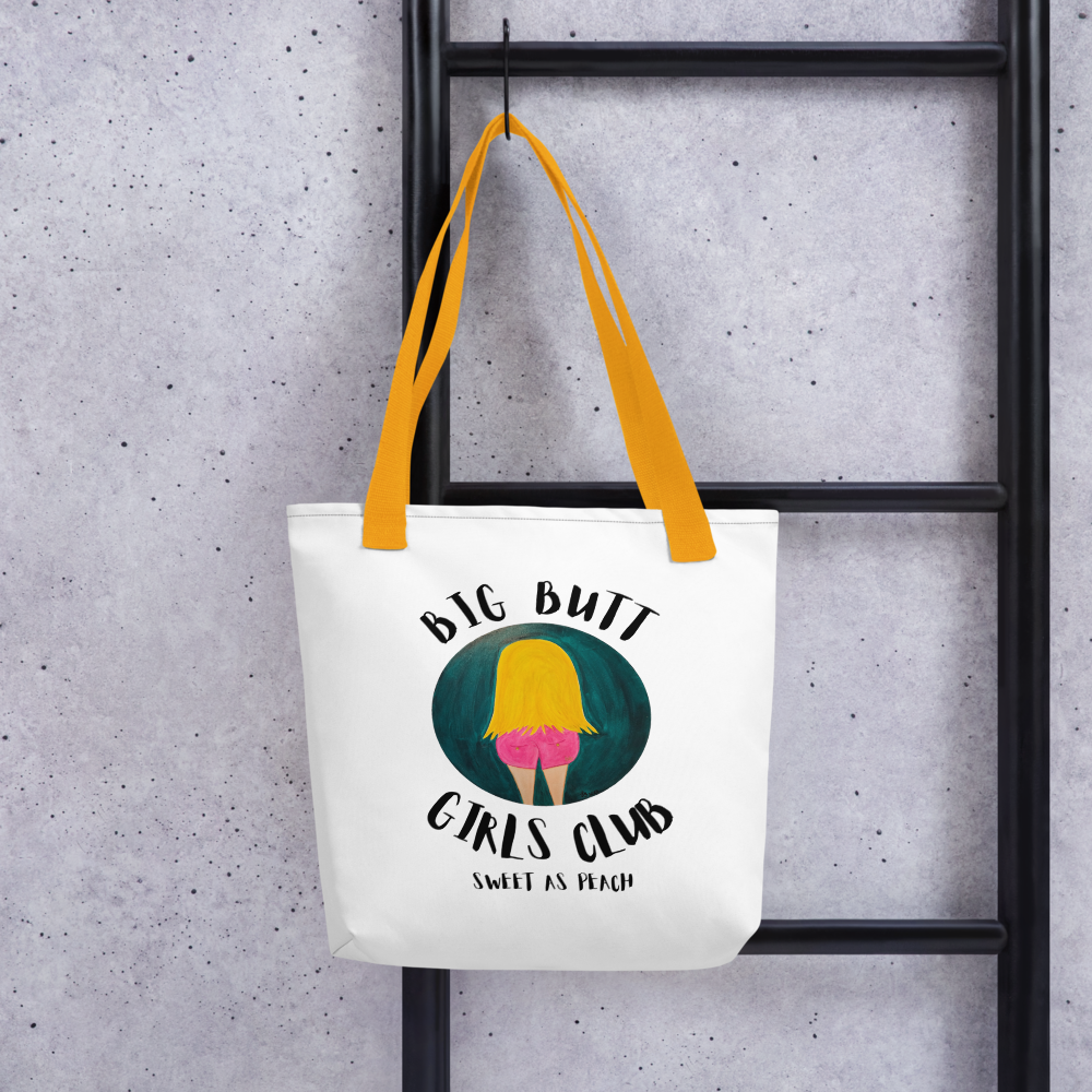 Tote bag with 'Big Butt Girls Club' graphic hanging on a black metal ladder against a gray concrete wall.