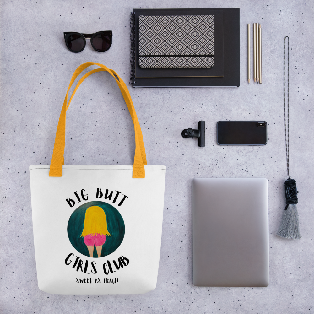Tote bag with 'Big Butt Girls Club' design on a gray surface with accessories.