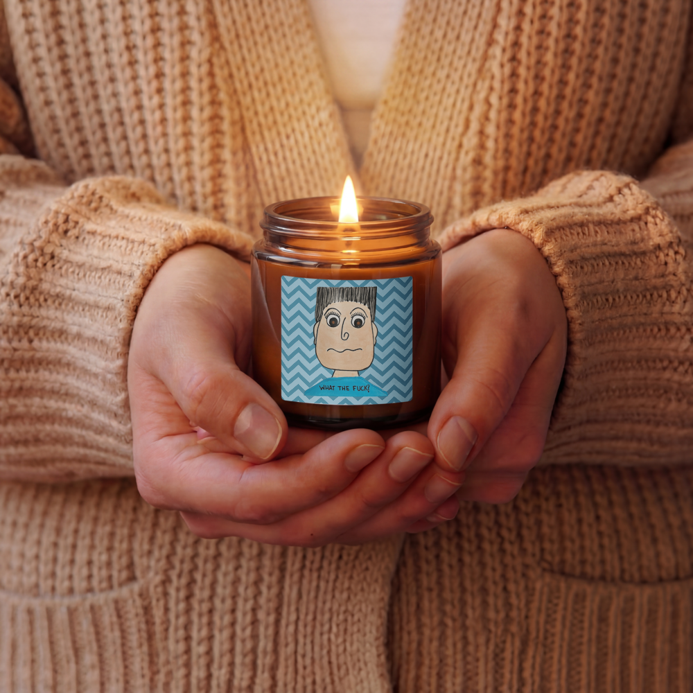 Person holding a lit candle in a brown jar with a label, wearing a beige sweater.