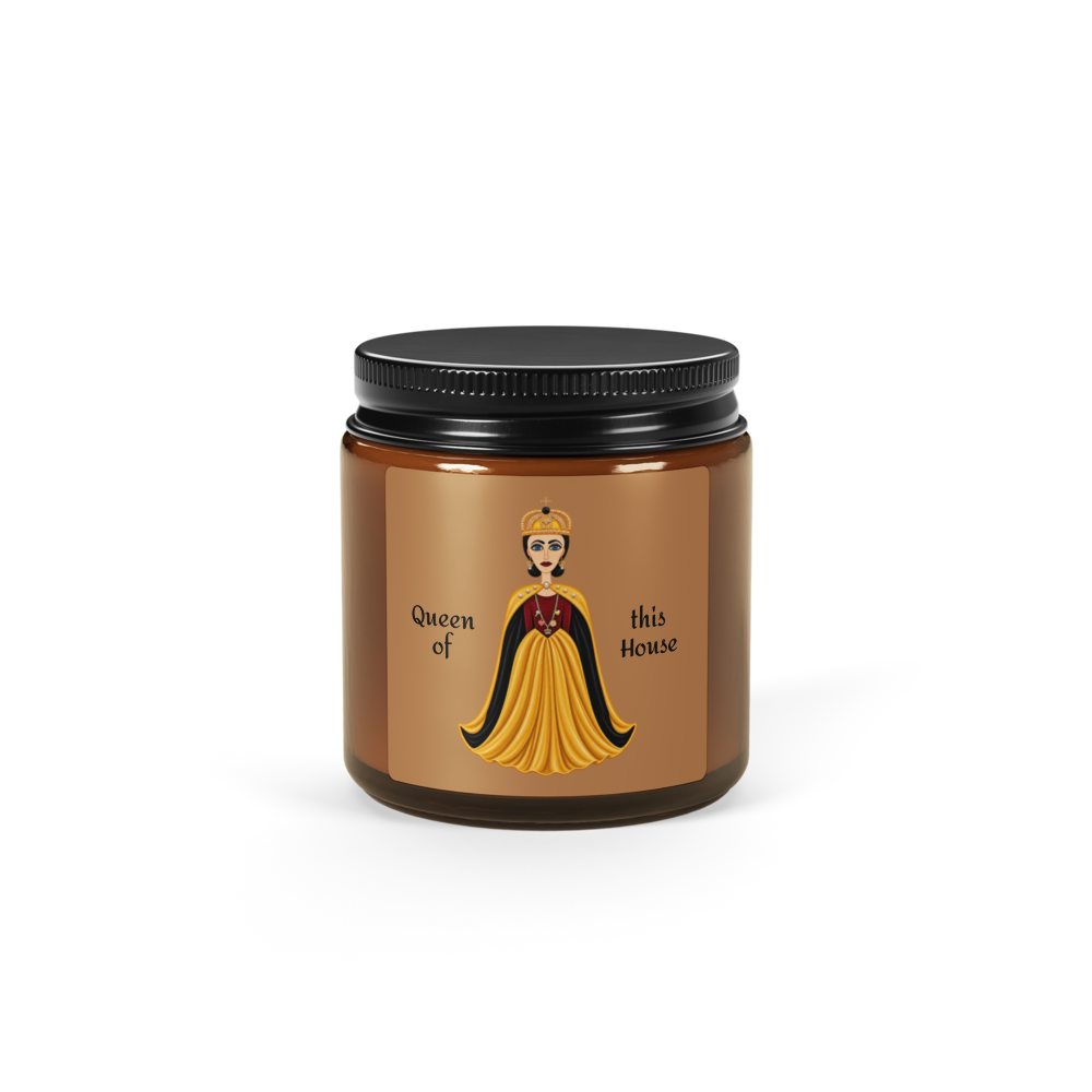 An amber glass jar candle with a black metal lid and a brown label featuring an illustration of a queen in a yellow gown and the text 'Queen of this House'.