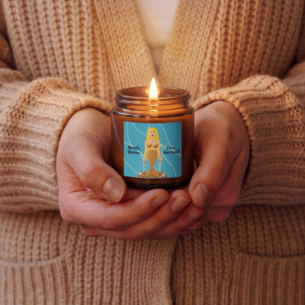 A person in a beige knit cardigan holds a lit amber glass jar candle with a blue label featuring a stylized figure and the text 'Black Magic' and 'I'm a sorceress.'.