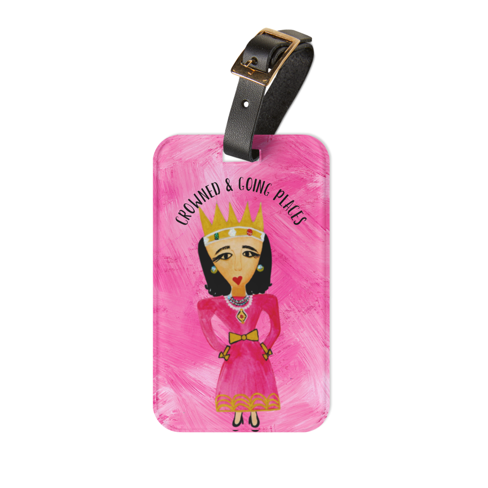A rectangular pink luggage tag with a black strap and gold buckle, featuring a hand-painted style illustration of a queen in a pink dress and gold crown, with the text 'CROWNED & GOING PLACES' above her.