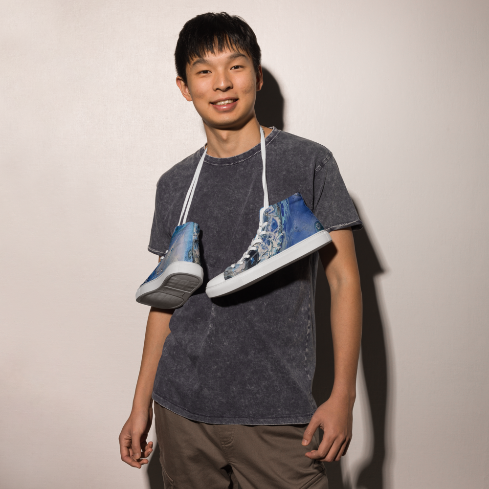 Person wearing a dark gray t-shirt with a graphic design, holding two sneakers with similar designs.
