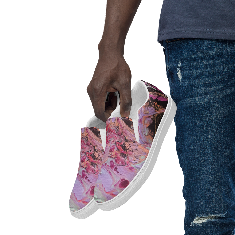 Person holding a pair of slip-on shoes with a colorful abstract design on a white background