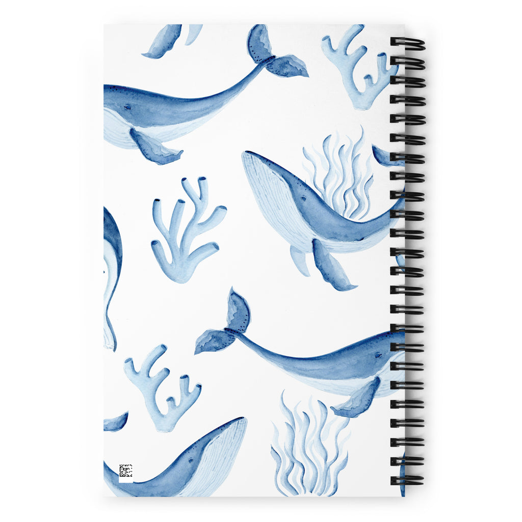 A spiral-bound notebook with a white cover decorated with blue watercolor illustrations of whales, coral, and seaweed, shown on a clean white background.