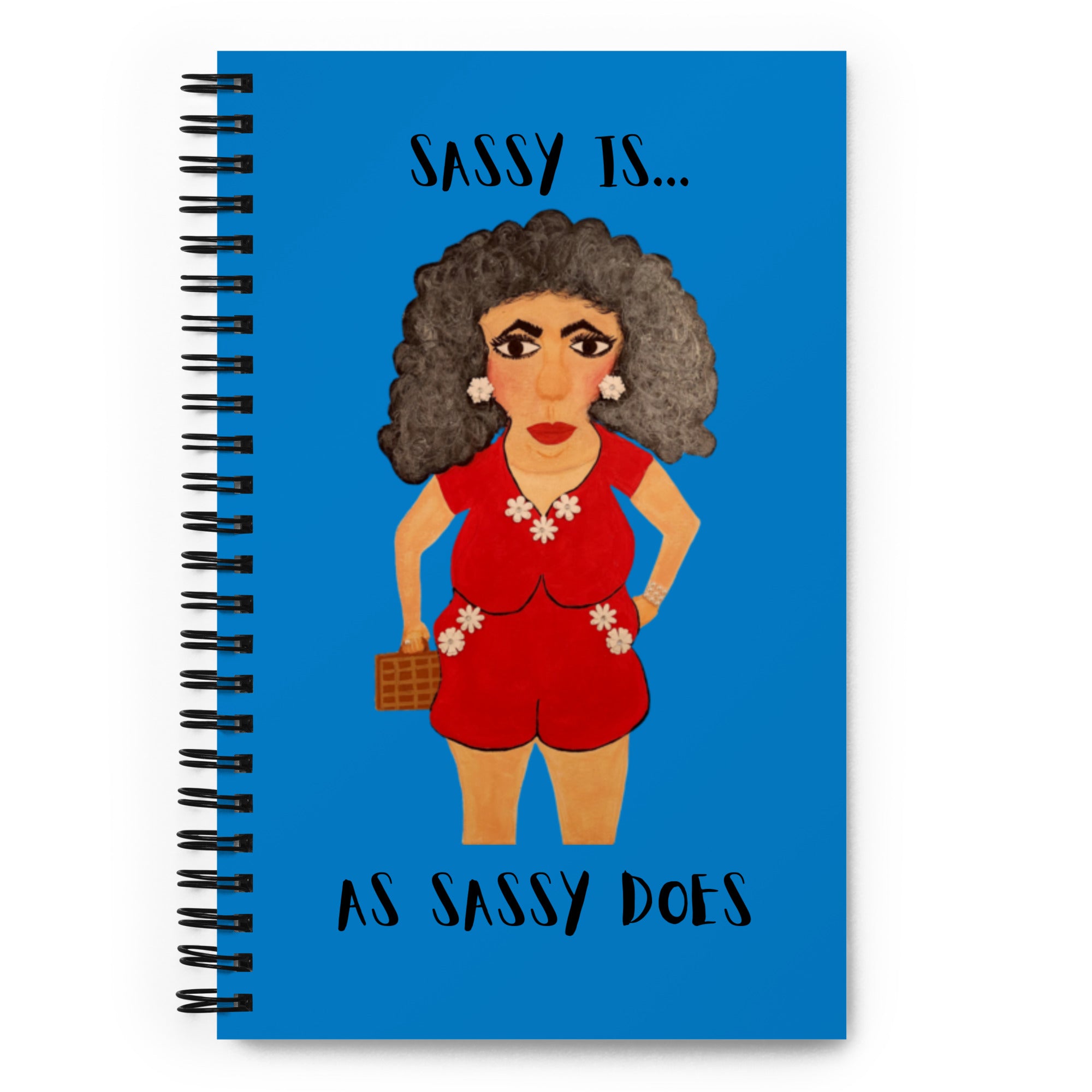 A spiral-bound notebook with a bright blue cover featuring an illustrated woman in a red outfit and the text 'SASSY IS.