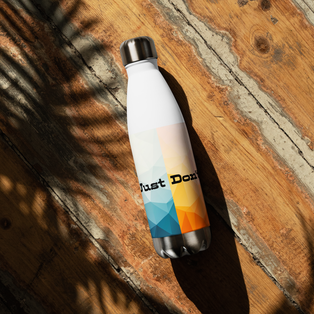 A white insulated water bottle with a silver metal cap and base, featuring a geometric color-blocked design in blue, yellow, and orange with the text 'Just Do It' printed on the front. The bottle is photographed diagonally on a rustic wooden surface with dappled sunlight and leaf shadows.