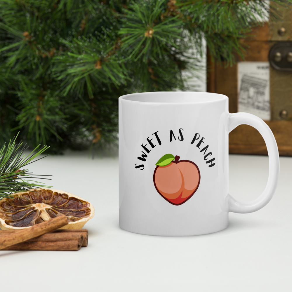 White mug with 'Sweet as Peach' design on a surface with decorative elements.