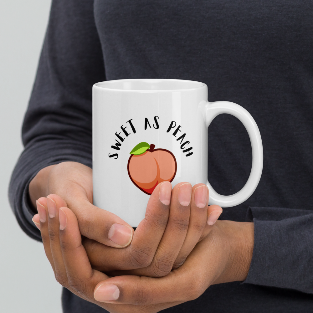 Person holding a white mug with 'Sweet as Peach' design against a gray background