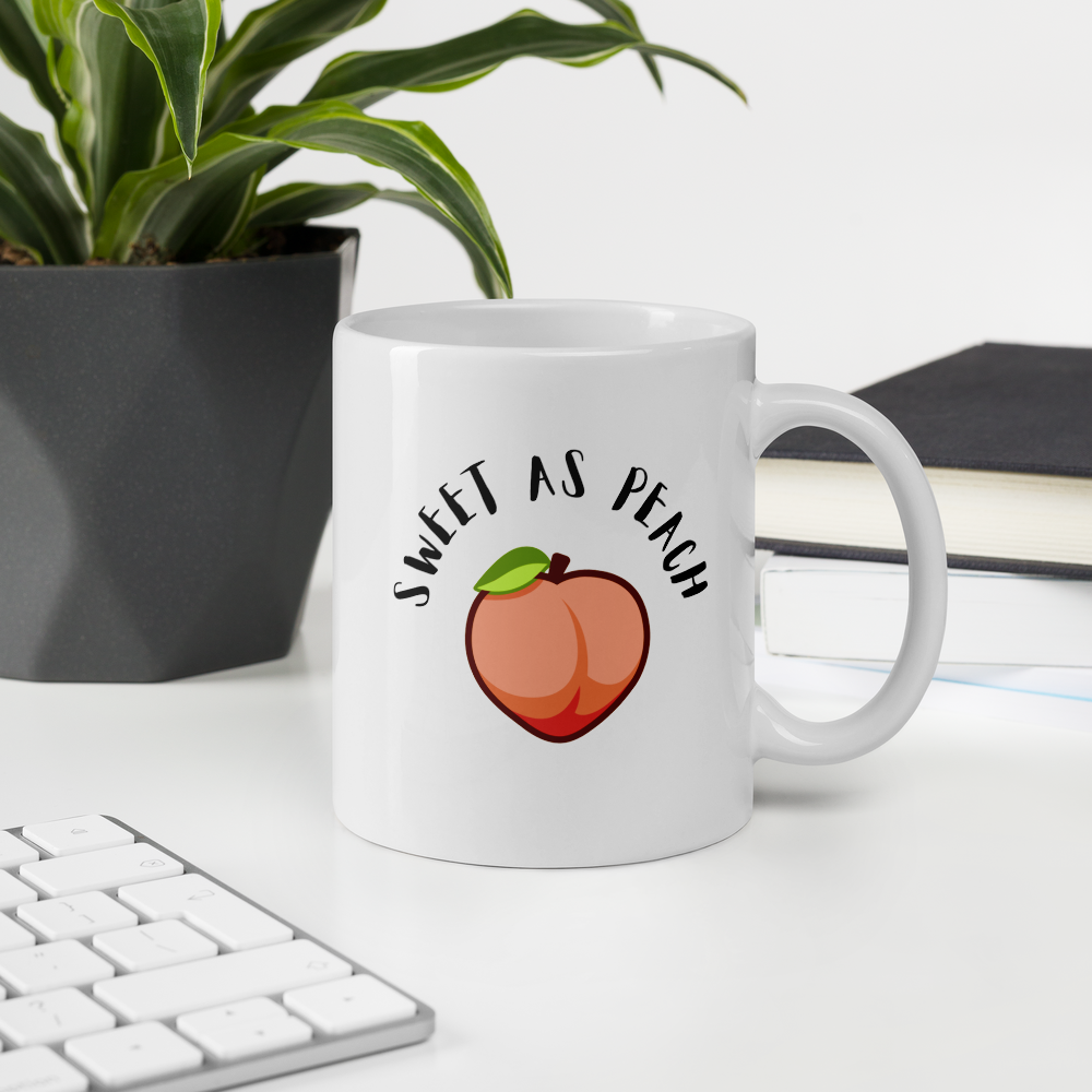 White mug with 'Sweet as Peach' design on a desk with a plant and books in the background