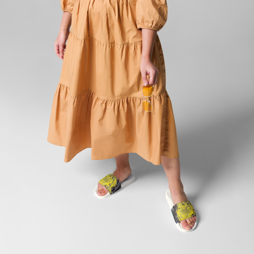 Person wearing a mustard yellow dress with white sandals on a gray background